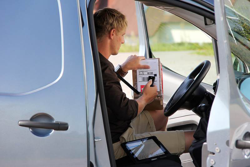 Man scanning parcel in the front of a van.